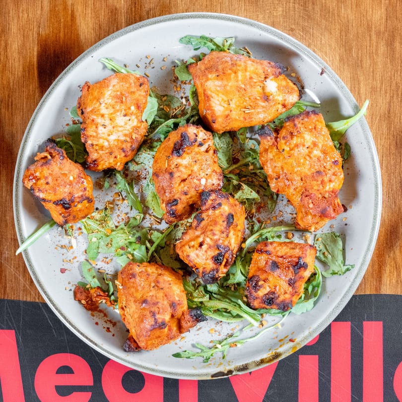 Grilled chicken pieces with spices and arugula on a plate, on a wooden table.