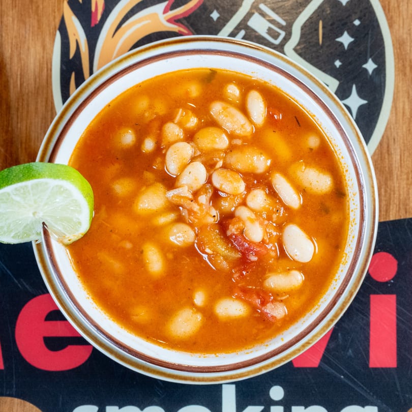 A bowl of white bean soup with a lime wedge on a patterned coaster.
