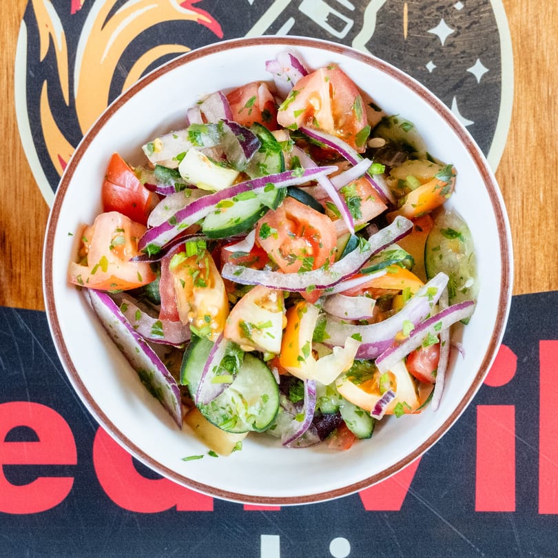 Overhead view of a fresh salad with chopped tomatoes, cucumbers, and red onions in a white bowl.