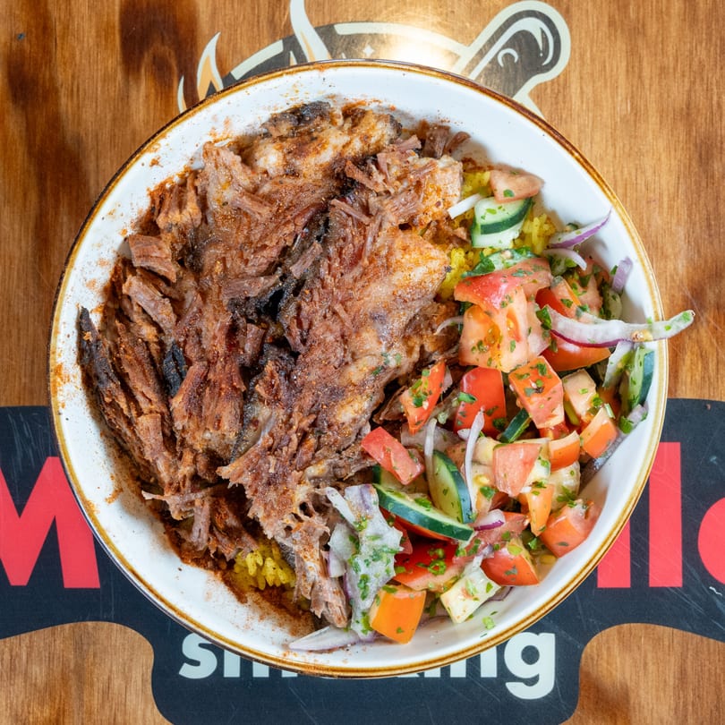Overhead view of a bowl with shredded meat, yellow rice, and a fresh tomato and cucumber salad.