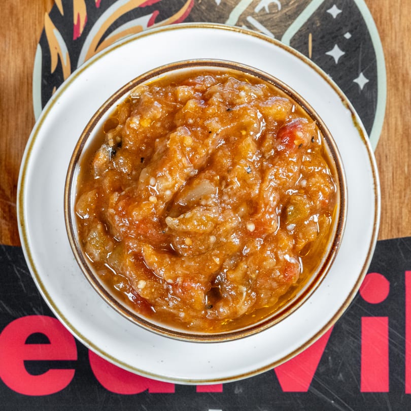 Overhead view of a bowl of chunky, orange-brown salsa or relish on a white plate.